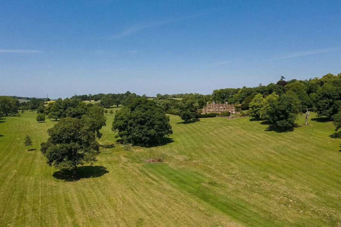 Aerial view across open parkland and specimen trees, with the house in the distance