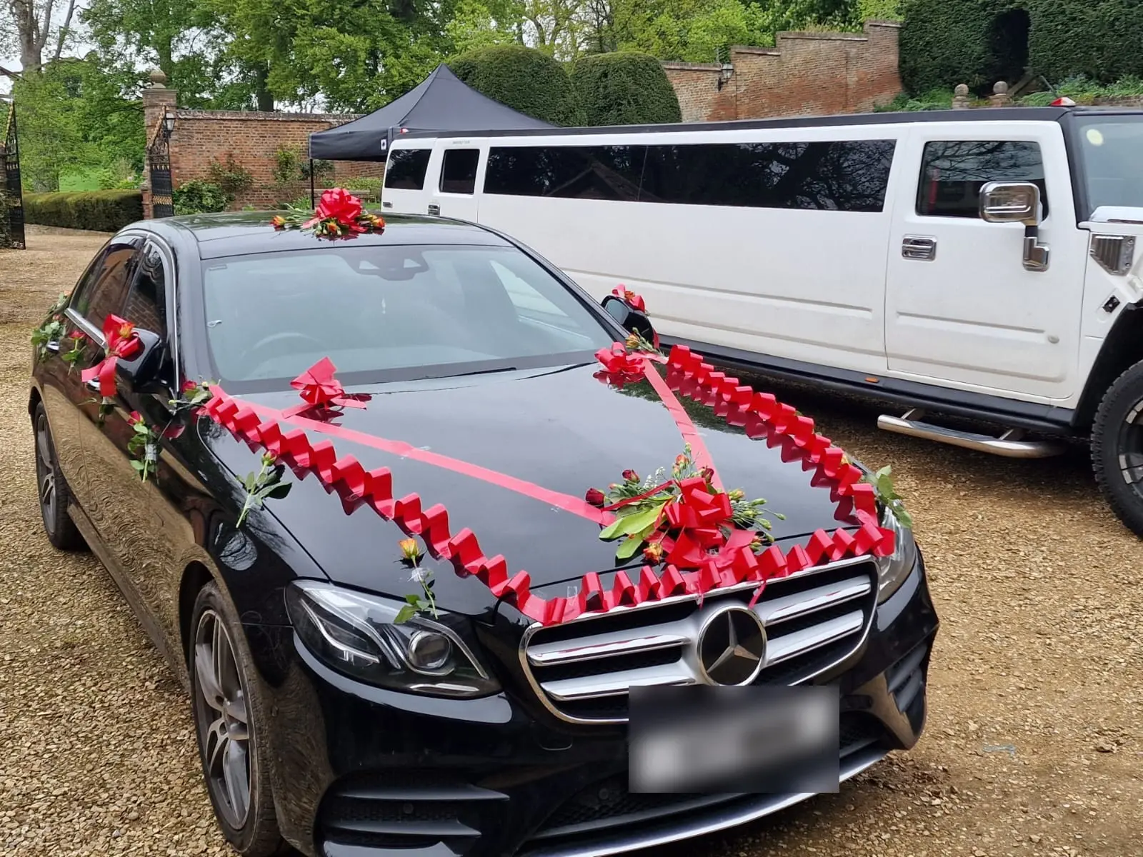 A ribbon-decorated car and a white stretch limousine on the gravel