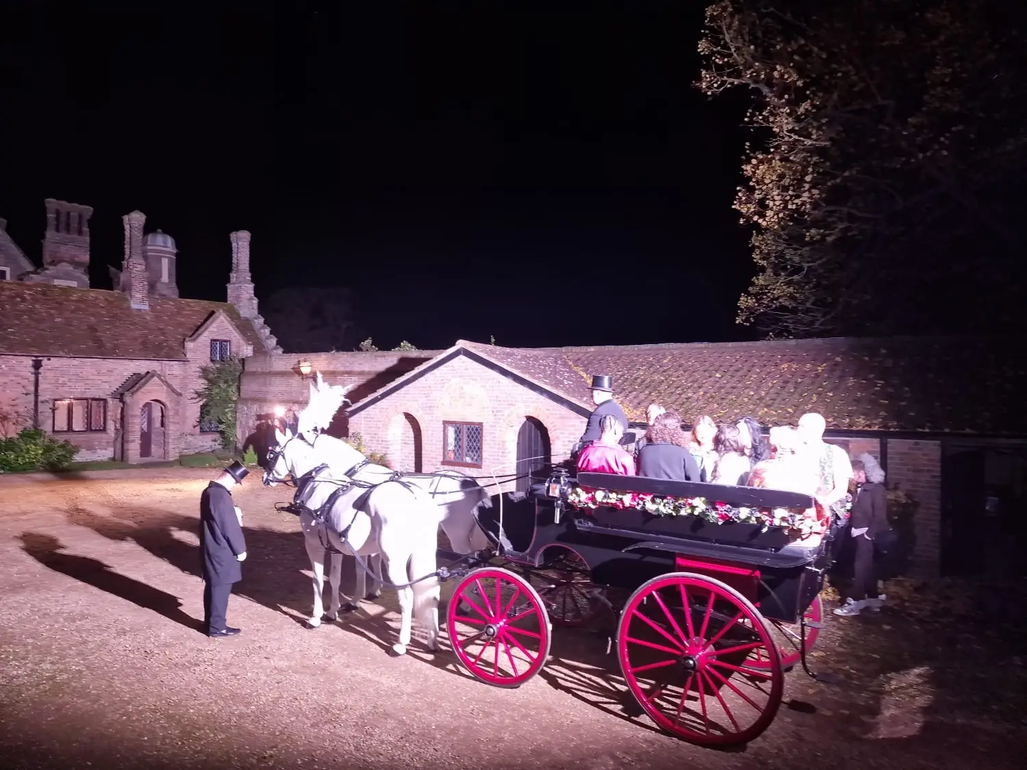 A horse-drawn carriage with white horses, lit in the courtyard at night
