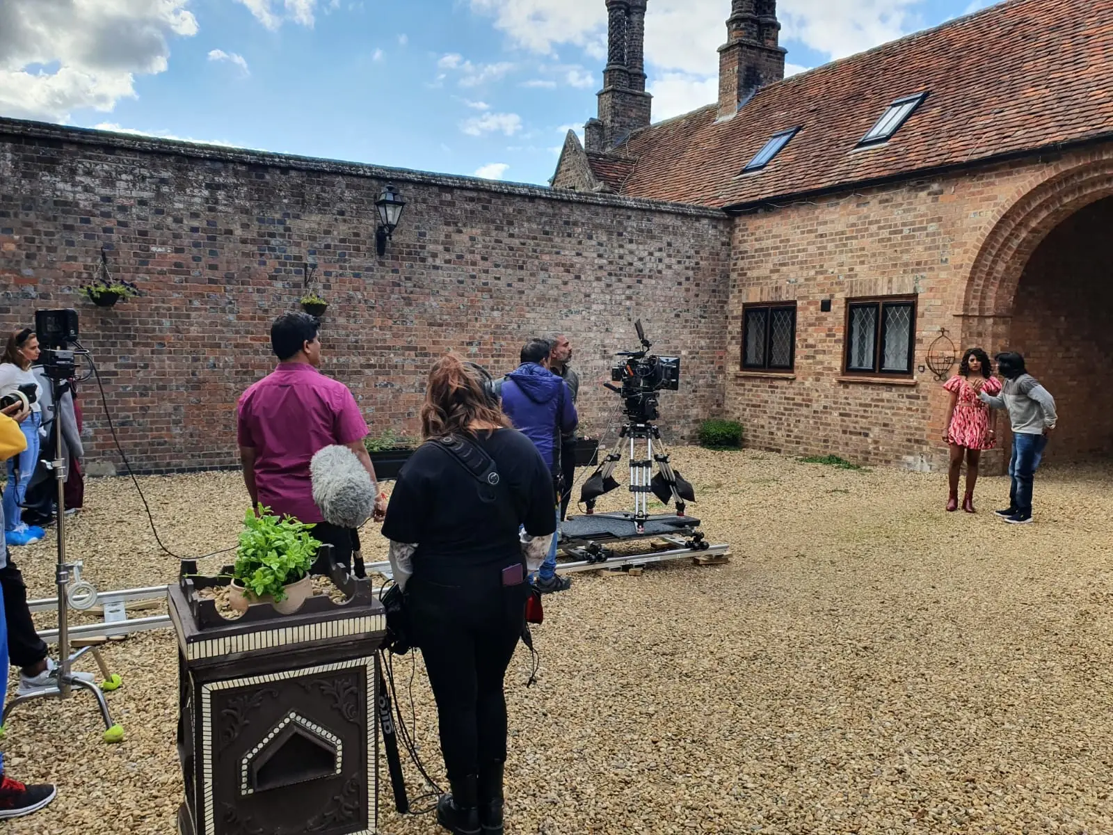 Crew filming in the gravel courtyard beside the brick archway