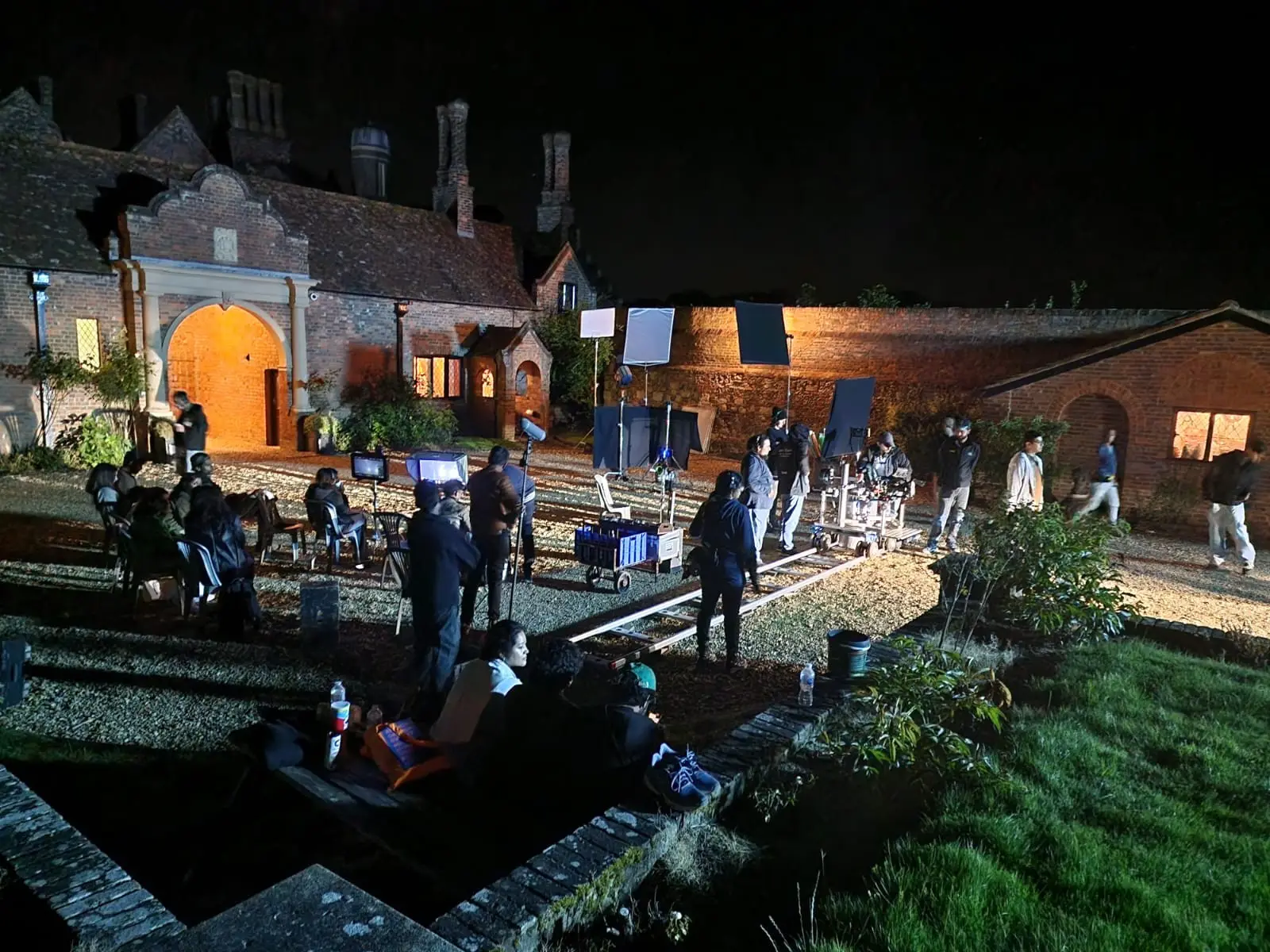 The courtyard and gatehouse at night, lit for filming, with crew, lamps and dolly track