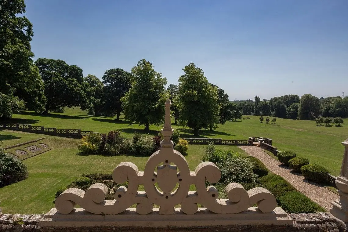 The formal garden and parkland seen over a carved stone finial on the balustrade