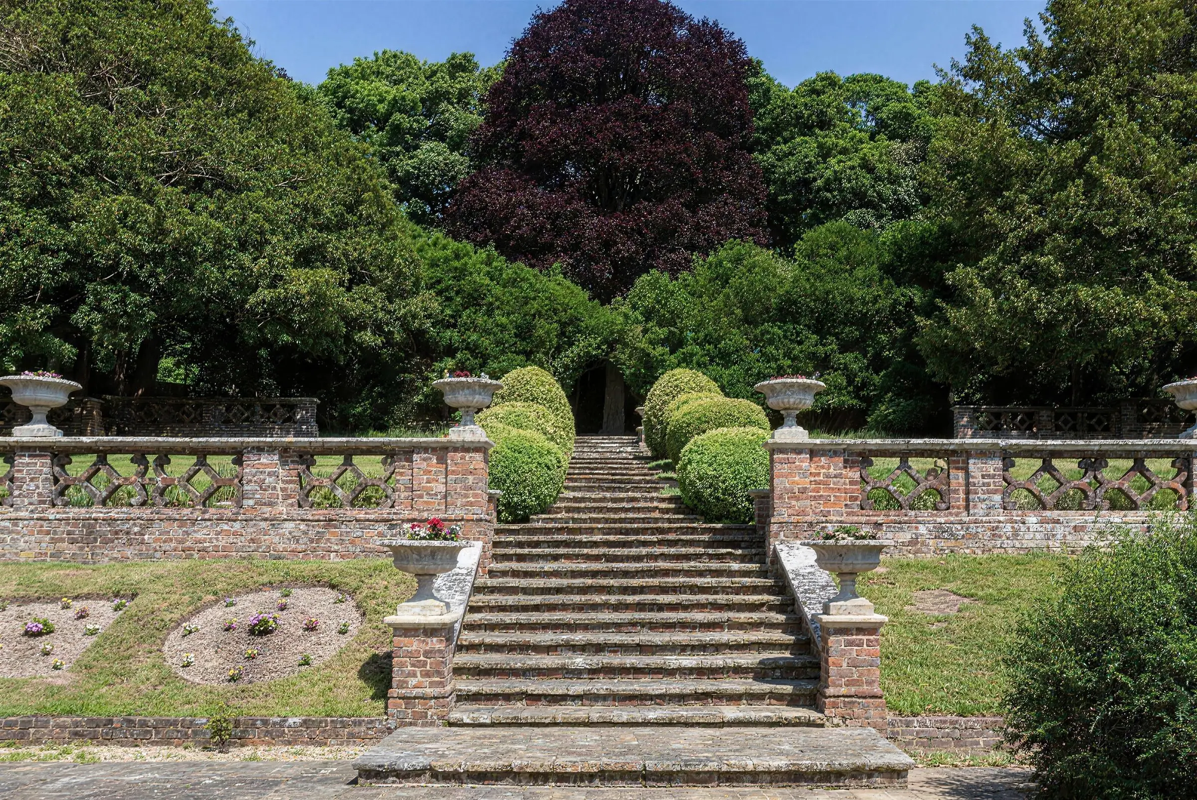 Stone steps rising between urns and clipped box, flanked by a pierced brick balustrade