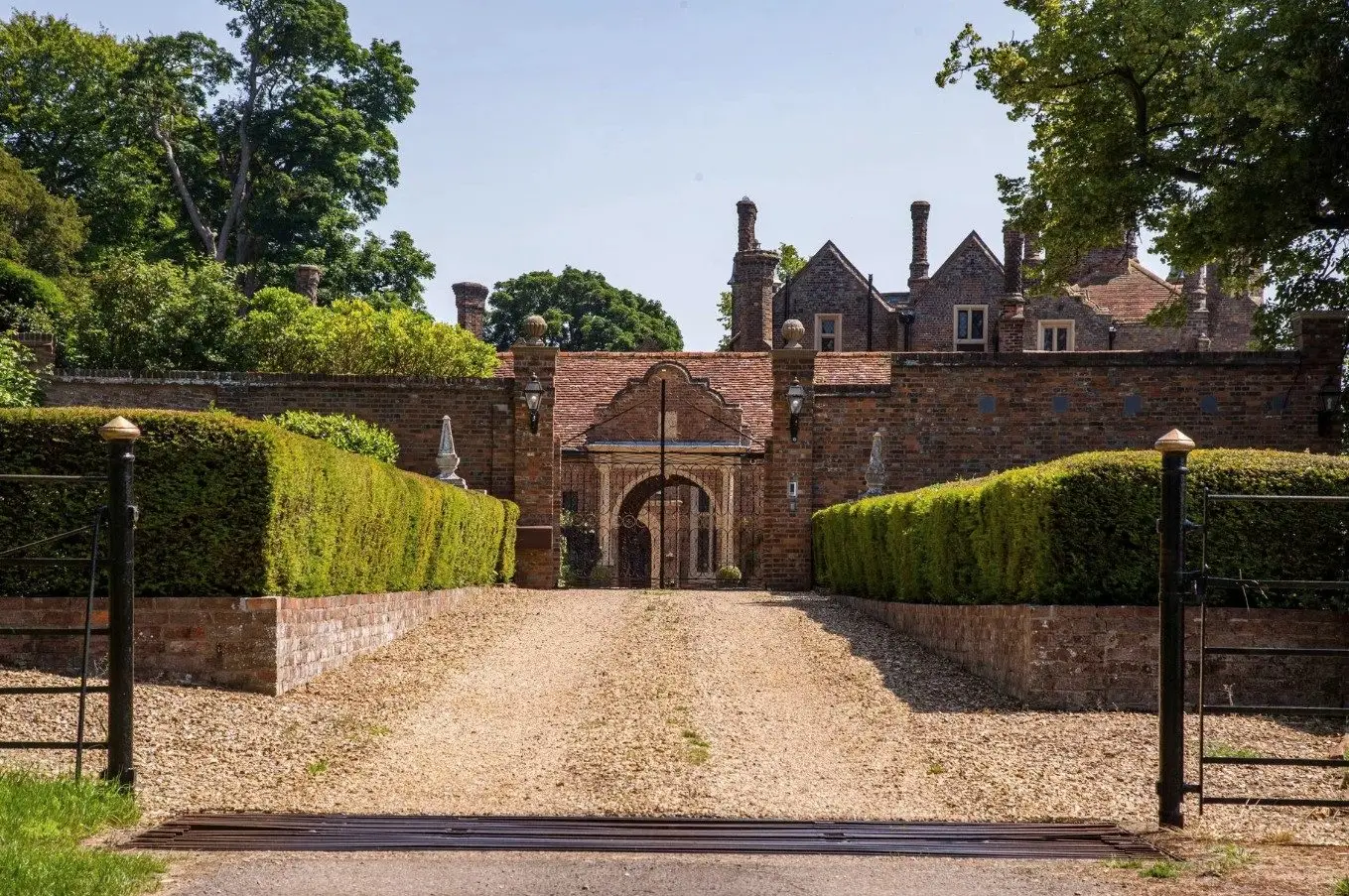 The gravel forecourt leading between clipped yew hedges to the arched gatehouse
