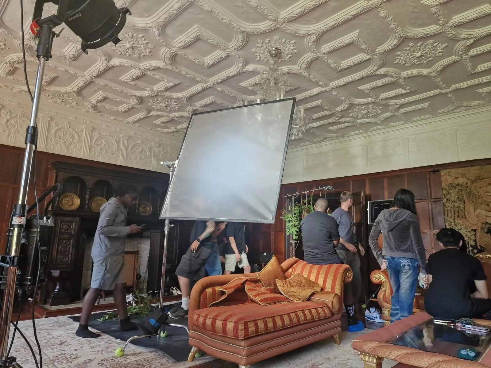 Crew setting lights in a panelled room with a moulded plaster ceiling and a striped day bed