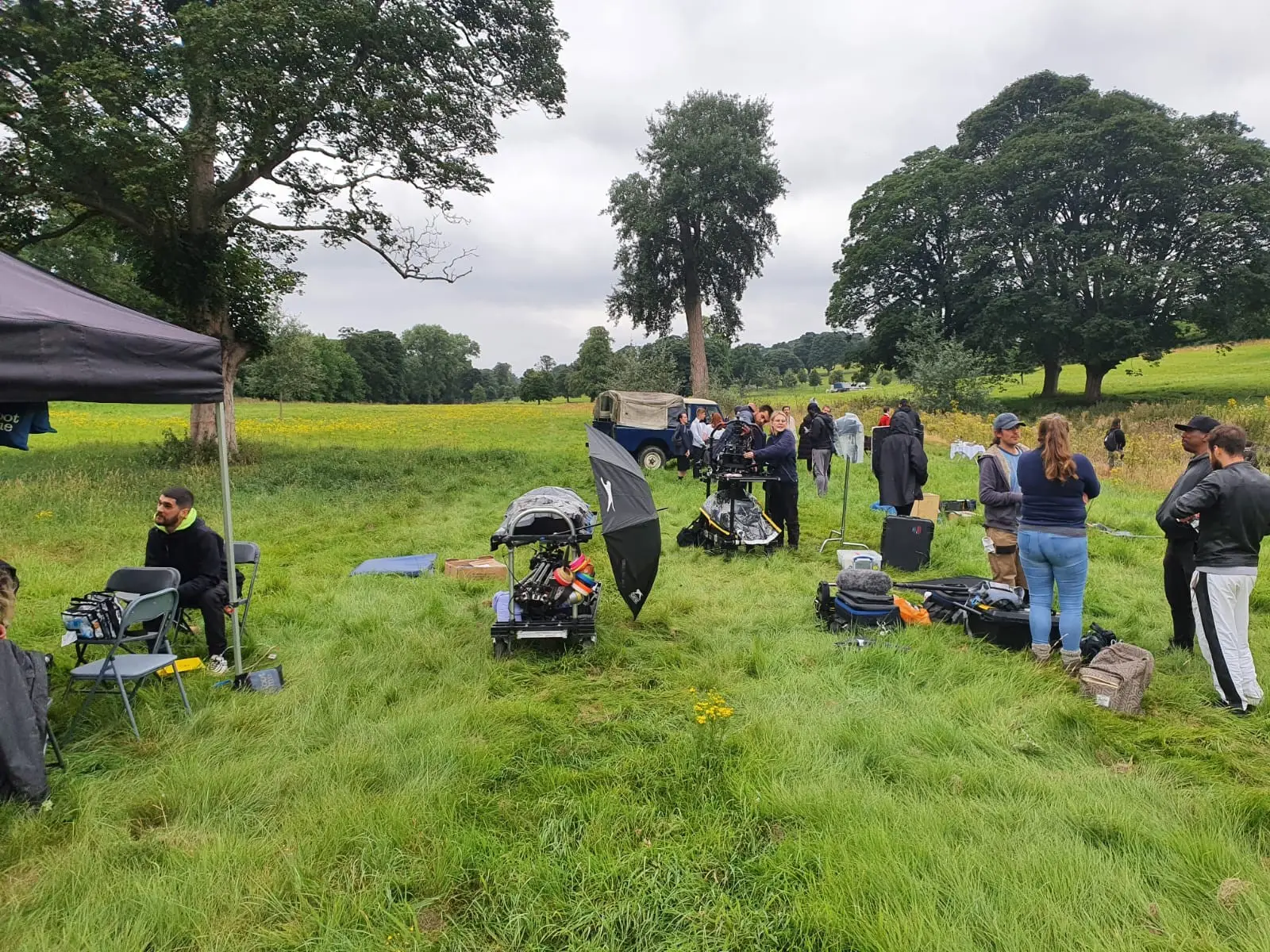 Crew and equipment in the long grass of the park, with mature trees beyond