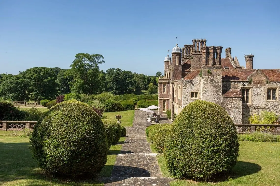 A stone path between two large clipped topiary domes, leading to the house